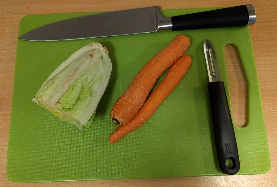 Cuchillo de cocina y pelador sobre una tabla de cortar
