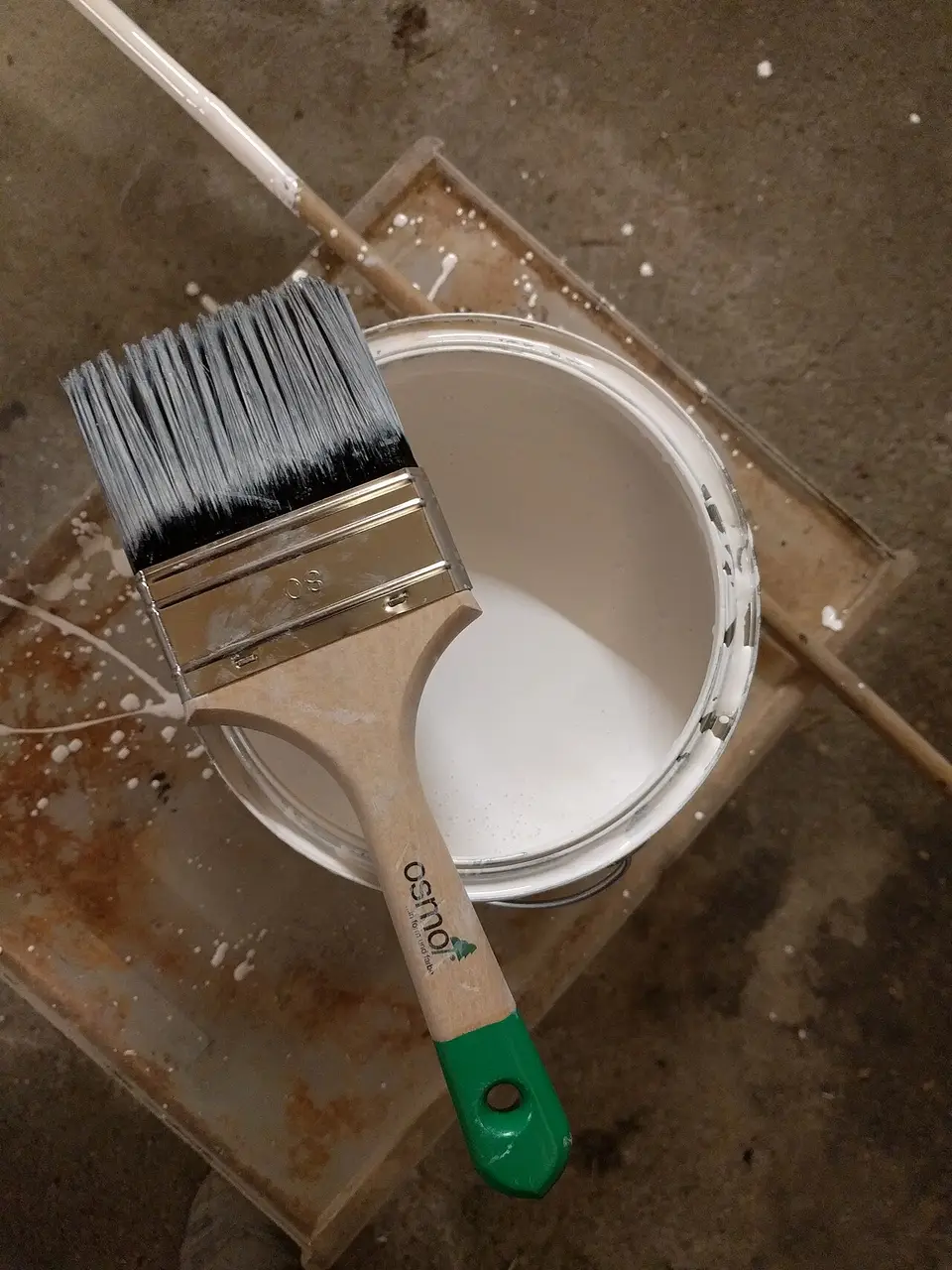 Brocha apoyada en un bote de pintura blanca