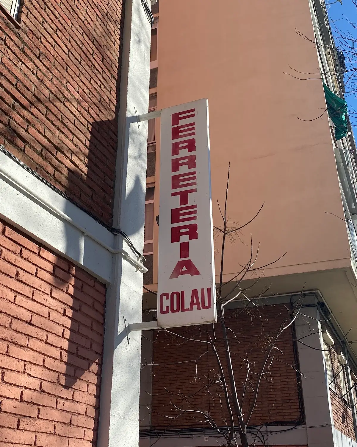 El rótulo vertical blanco con letras rojas, Ferretería Colau, colgado en la esquina de ladrillo de la tienda